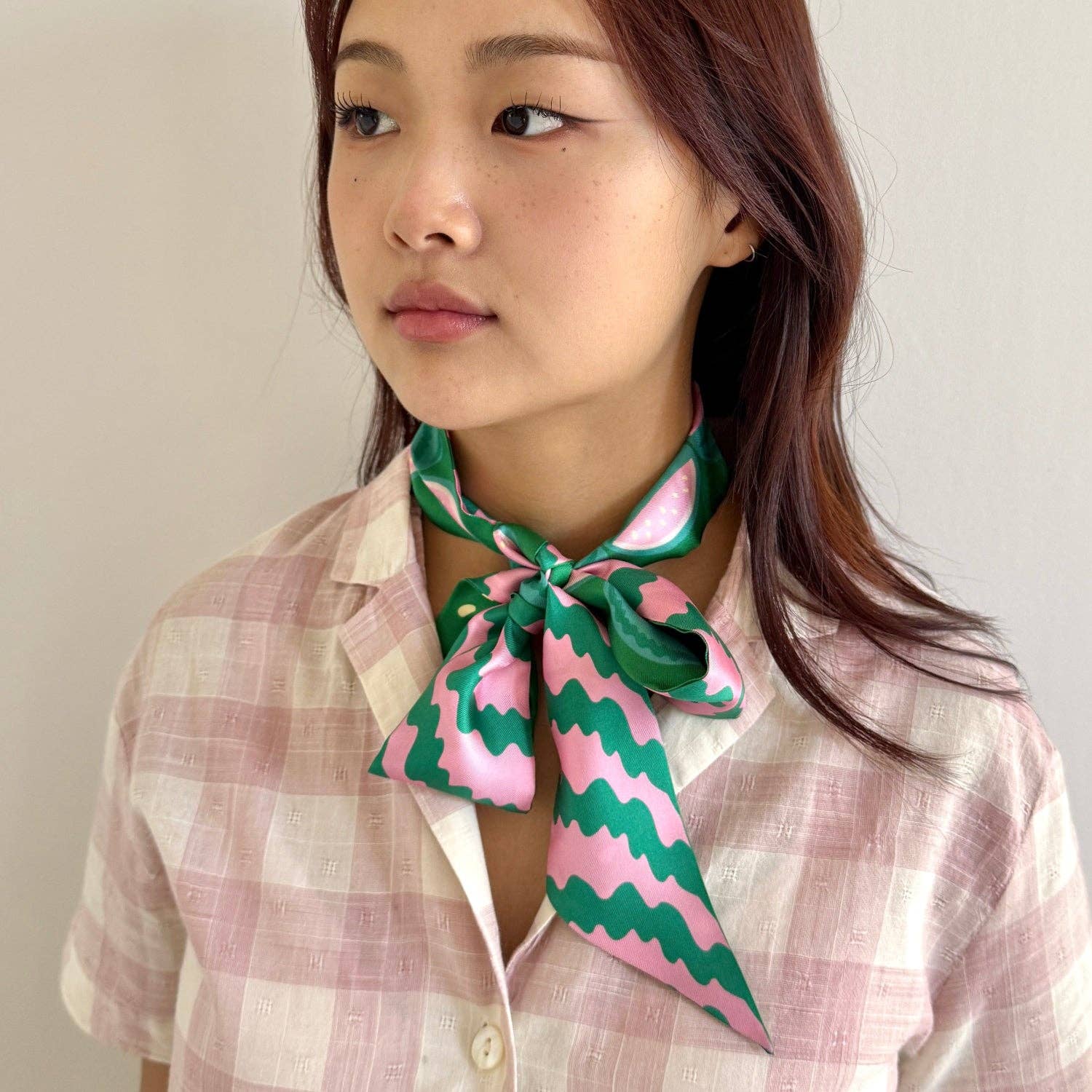 Woman wearing a pink and green patterned scarf around her neck against a plain background