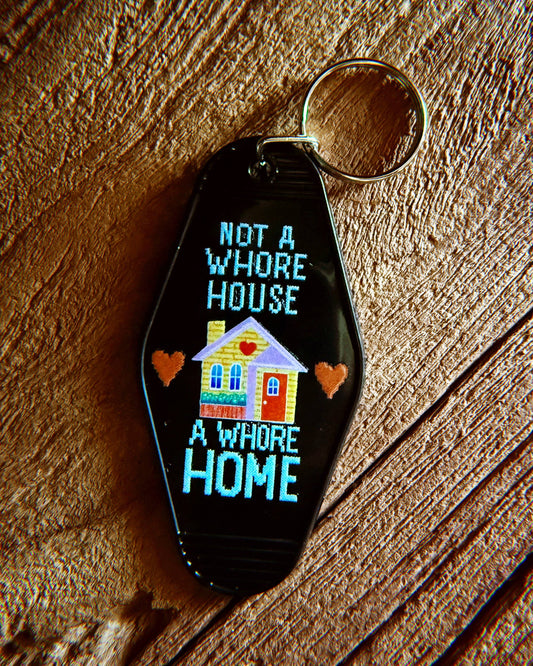 Keychain with text 'Not a Whore House, A Whore Home' on a wooden surface