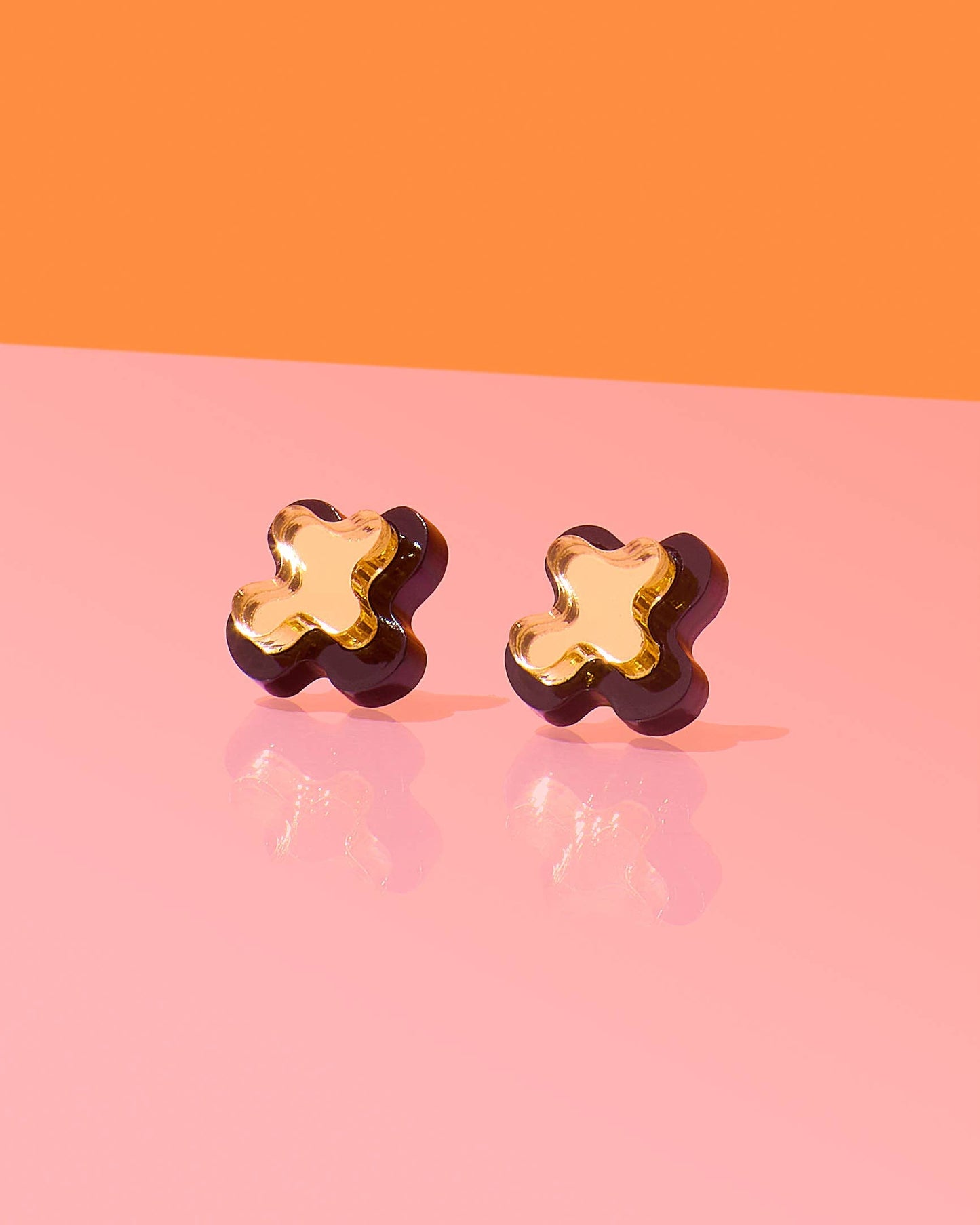 Pair of gold flower-shaped earrings on a pink and orange background