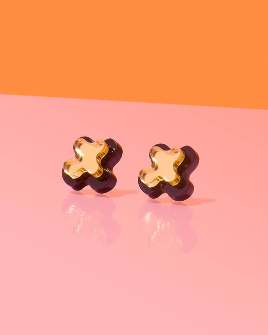 Pair of gold flower-shaped earrings on a pink and orange background