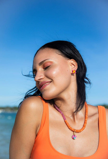 Woman wearing an orange tank top and colorful necklace with a blue sky background