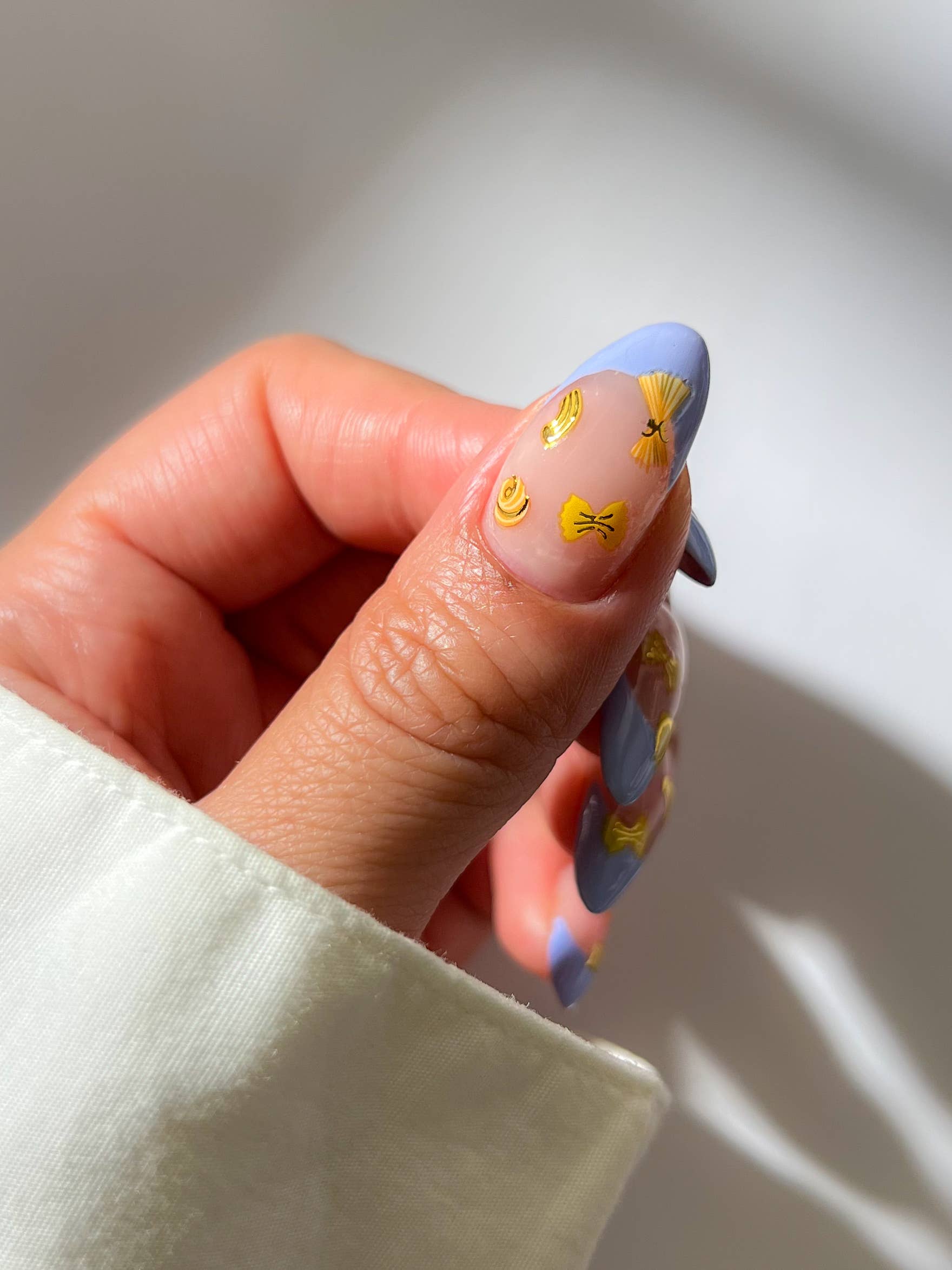 Hand with blue nail polish featuring yellow pasta designs on a neutral background, Al Dente Pasta Nail Art Stickers