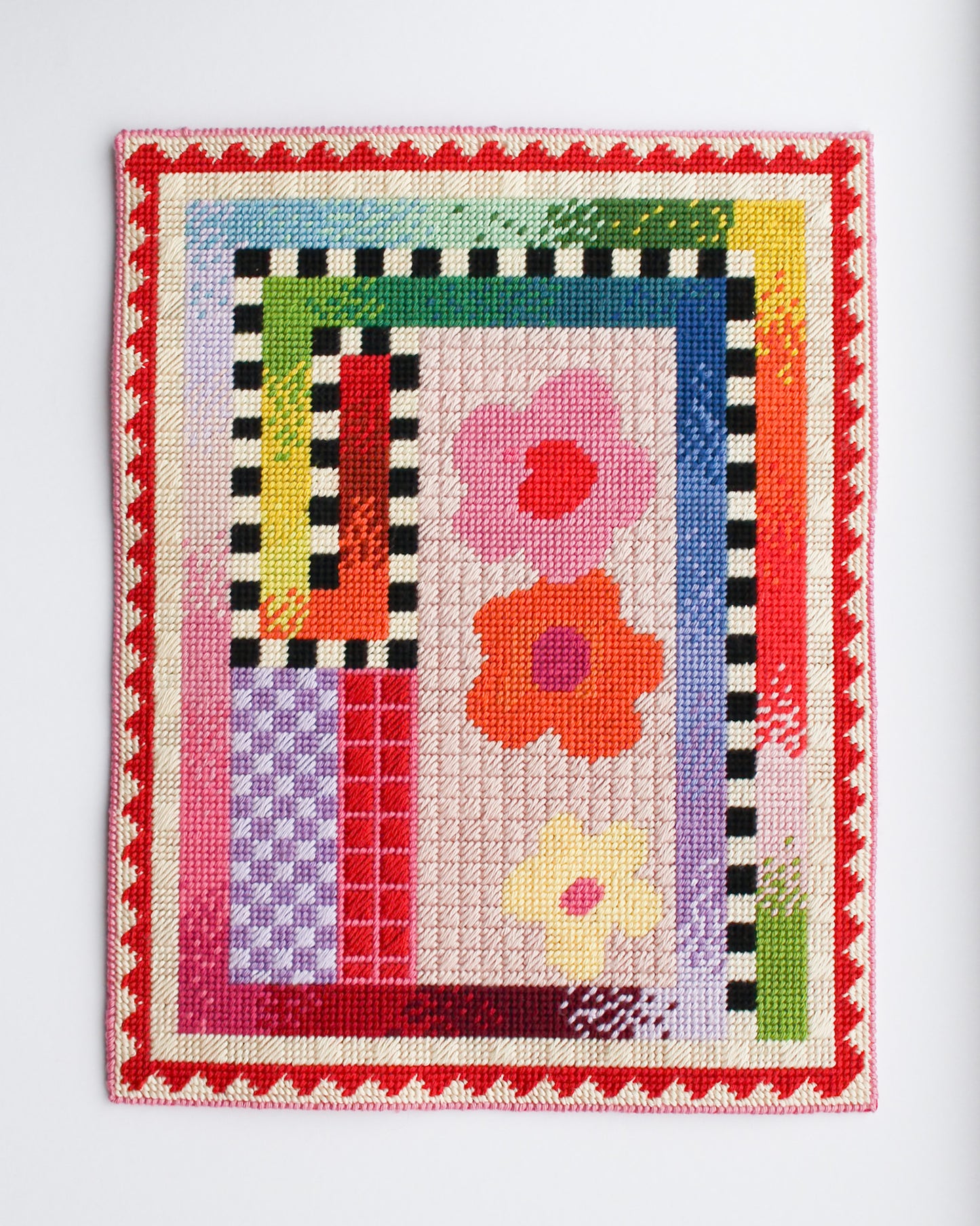 Colorful cross-stitched sampler with flowers and geometric patterns on a white background