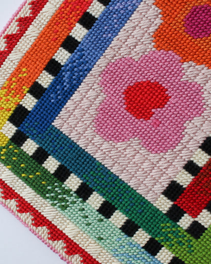 Close-up of a colorful embroidered fabric with geometric patterns and a pink flower.