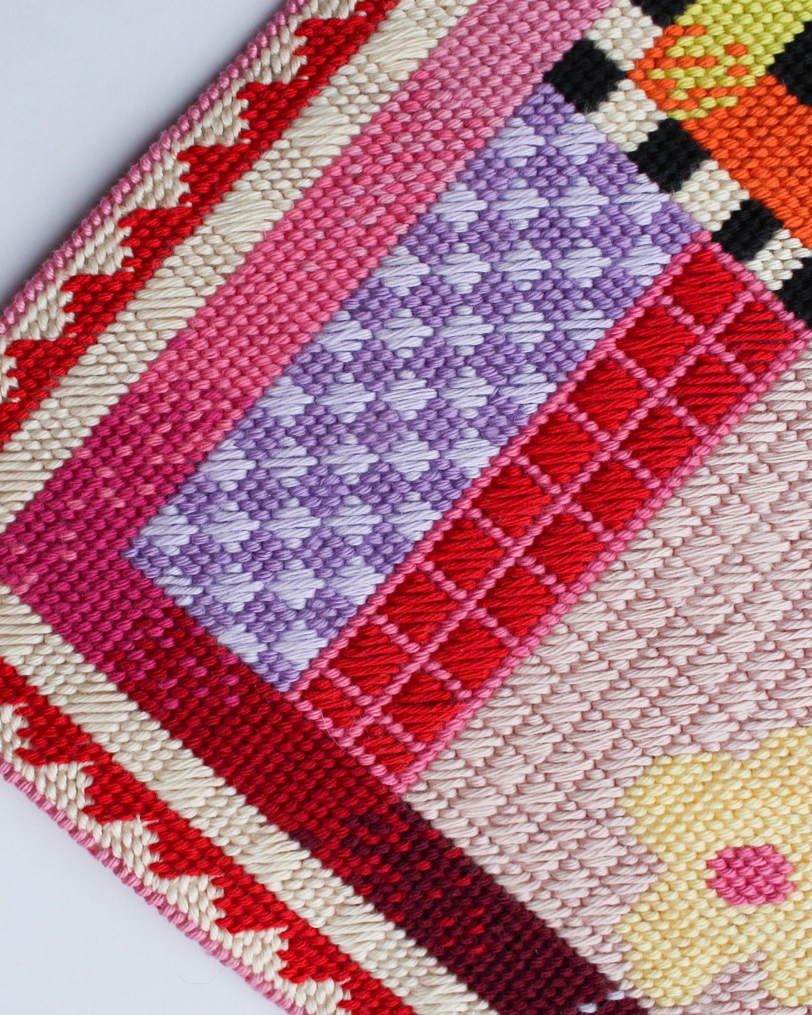 Close-up of a cross-stitched fabric with geometric patterns in red, purple, pink, and yellow.