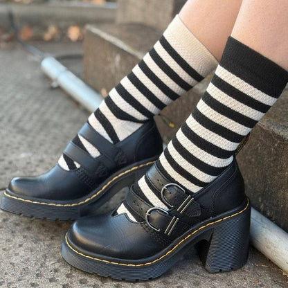 Black Mary Jane platform boots with double buckle straps, worn with black and cream striped knee-high socks on a concrete step.