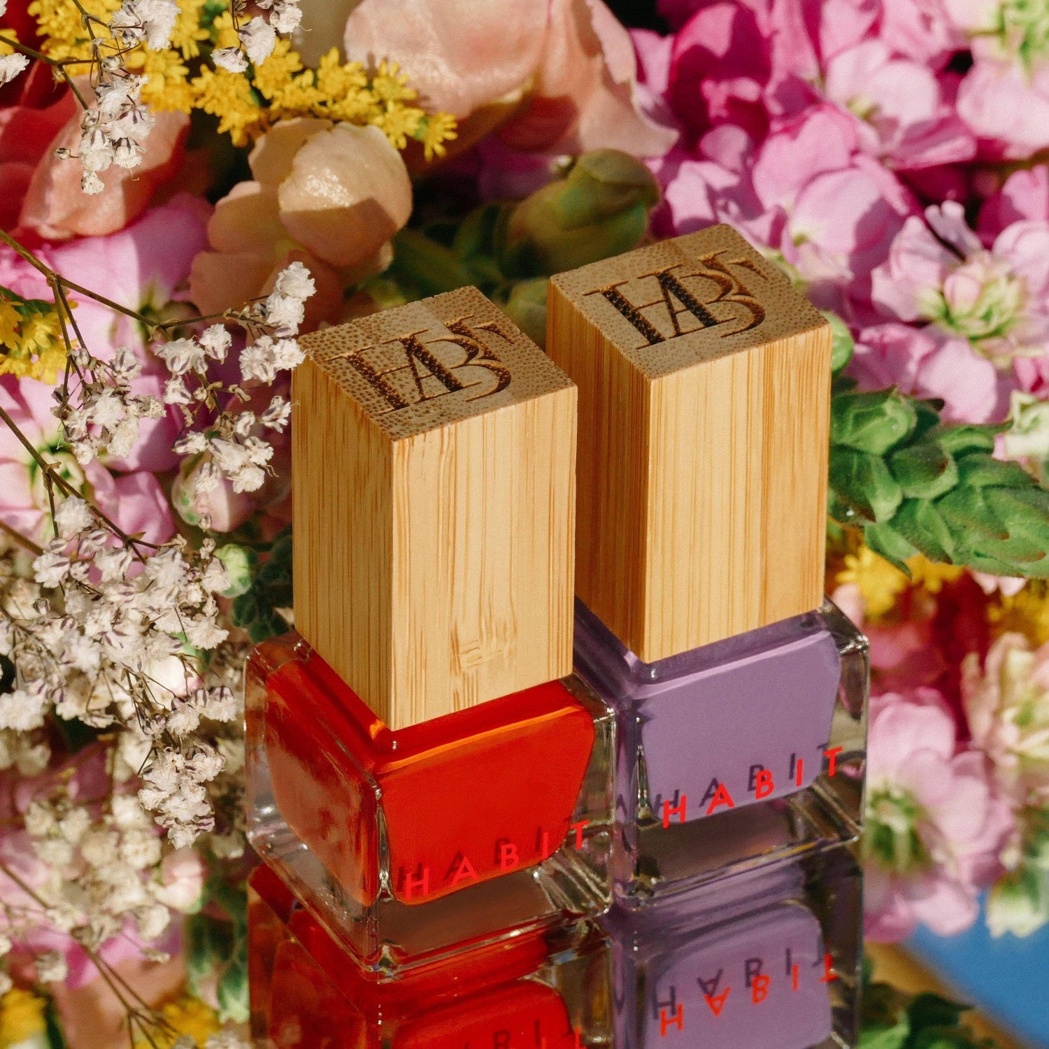 Two nail polish bottles stacked with flowers in the background, Belladonna Purple Toxin Free Nail Polish