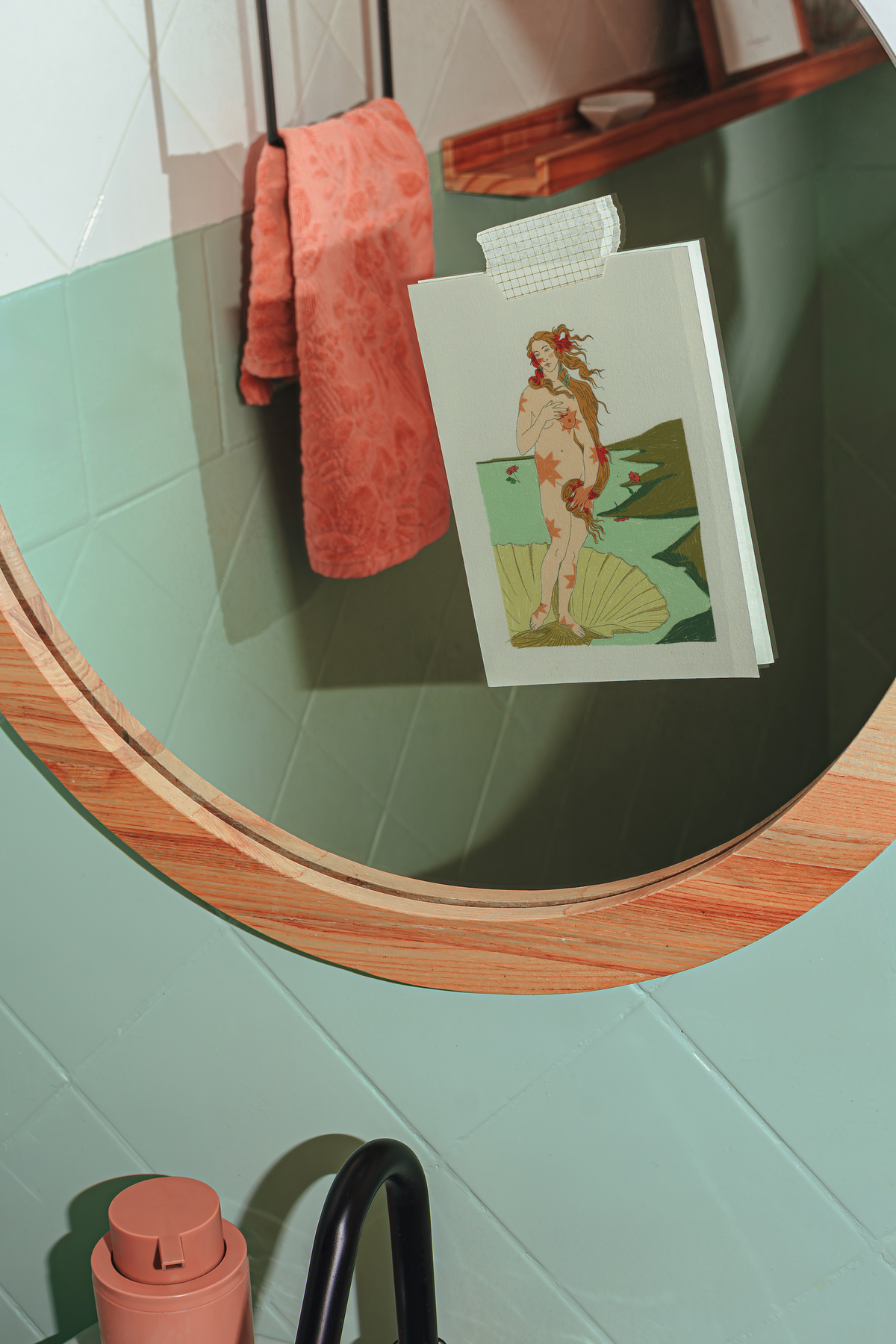 A rectangular art print with an Art Deco style illustration of a woman on a shell, taped to a bathroom mirror with a checkered tape. The print is displayed in a bathroom setting with a green tiled wall, a wooden-framed mirror, and a coral towel.