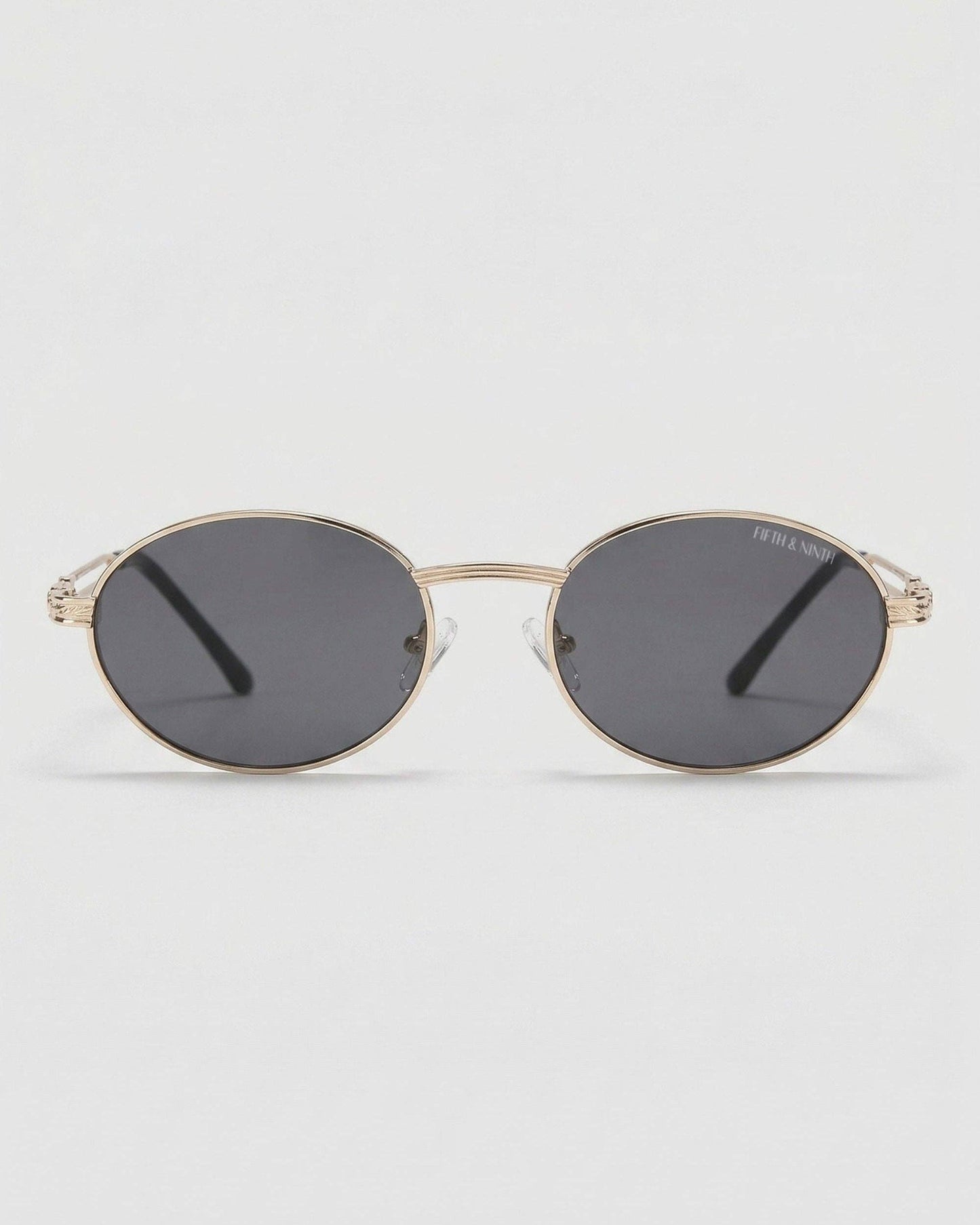 Gold-framed sunglasses with dark lenses on a light gray background