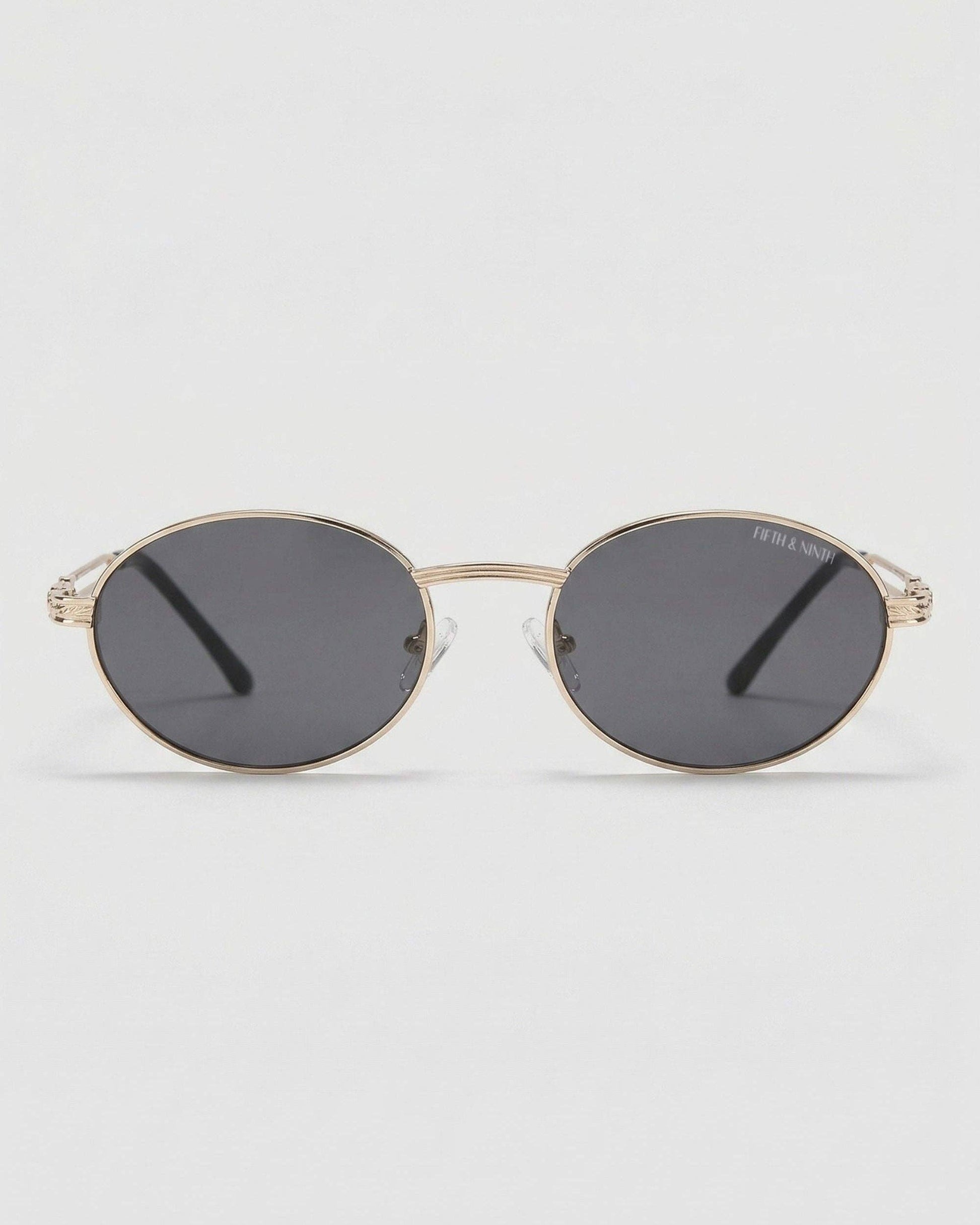 Gold-framed sunglasses with dark lenses on a light gray background