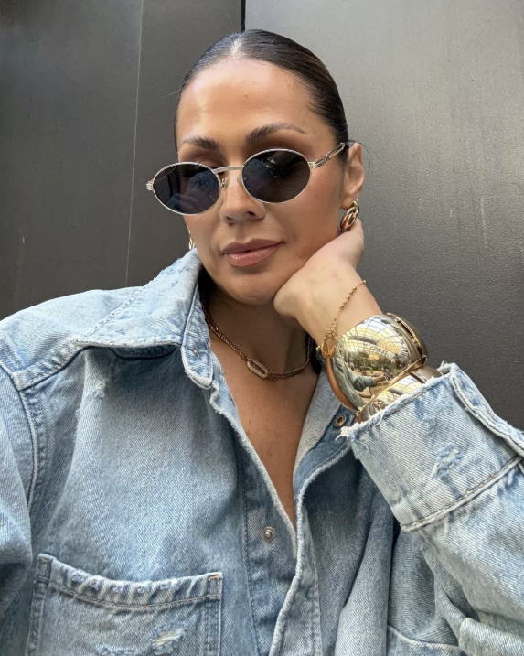Woman wearing sunglasses and a denim jacket against a plain background