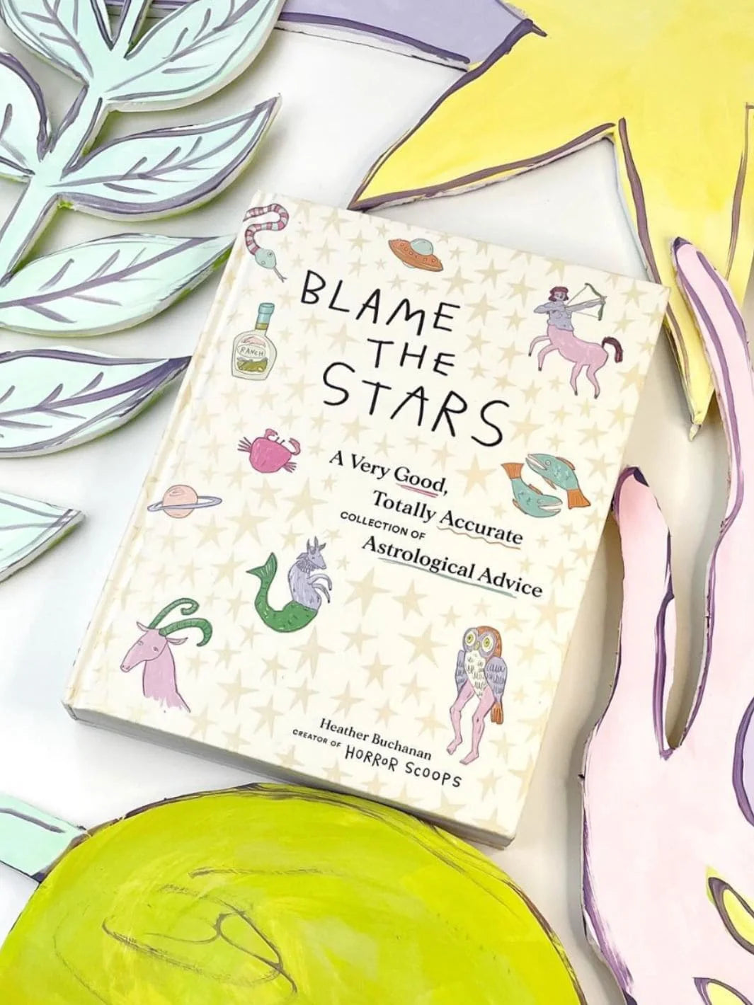 Book titled 'Blame the Stars' surrounded by colorful paper cutouts on a white background