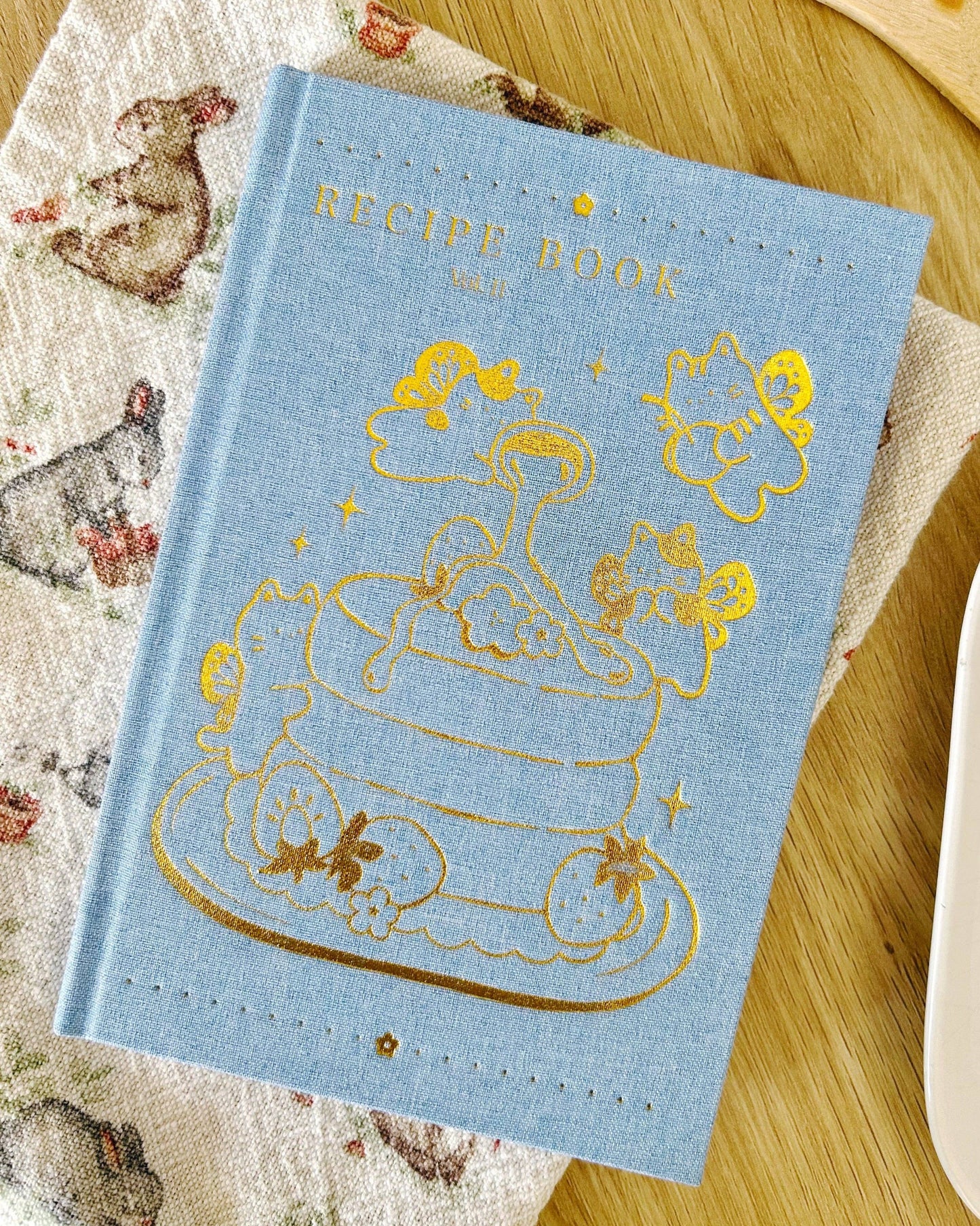 Blue recipe book with gold illustrations on a wooden surface
