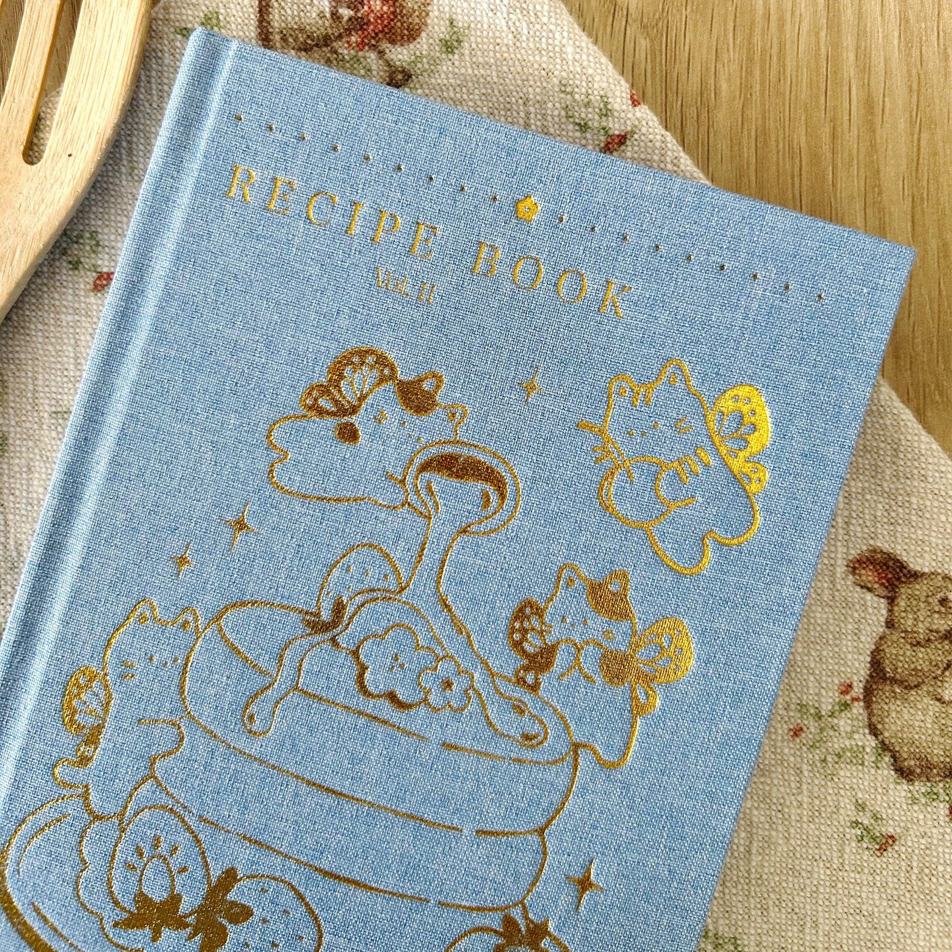 Blue recipe book with gold illustrations on a wooden surface, Blue Linen Recipe Book