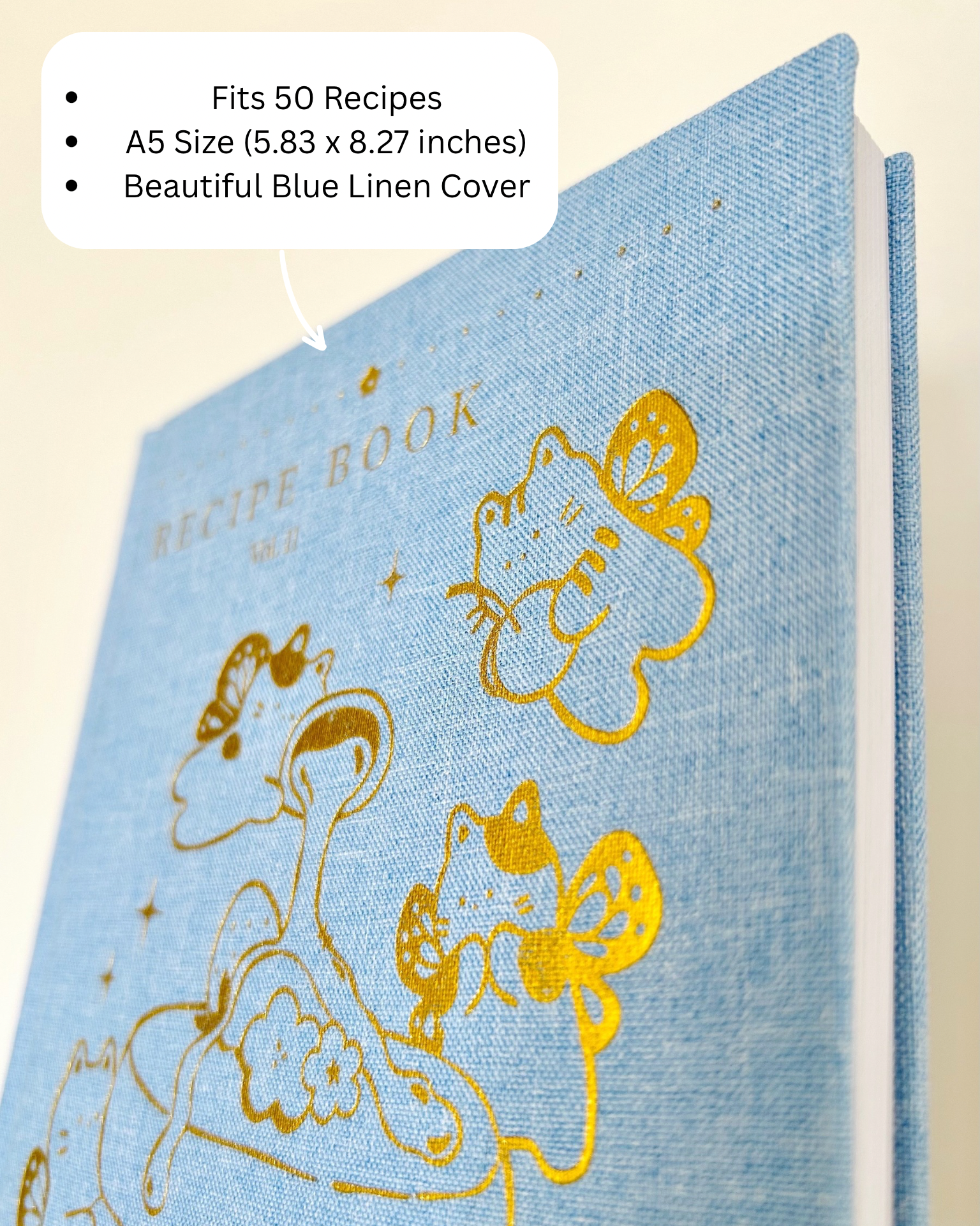 Blue linen recipe book with gold illustrations on a beige background