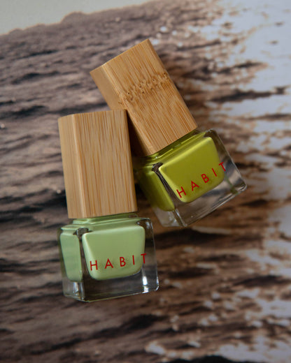 Two green nail polishes with bamboo caps on a wooden surface