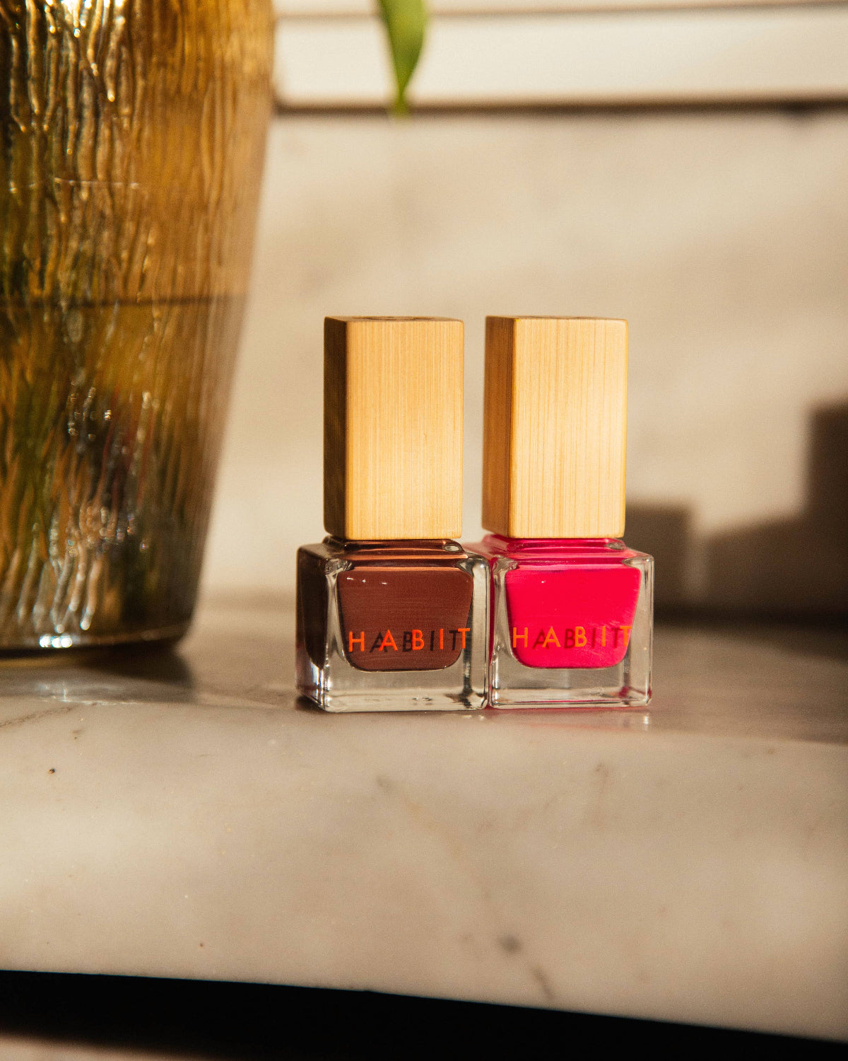 Two nail polish bottles with wooden caps on a marble surface, one brown and one pink, with a blurred background. Brownie Points Brown Toxin Free Nail Polish