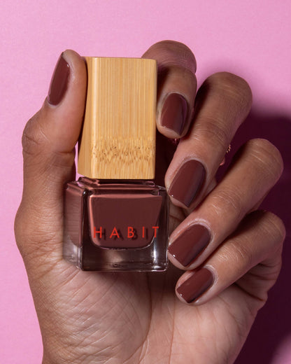 Hand holding a red nail polish bottle with 'Habit' branding against a pink background. Brownie Points Brown Toxin Free Nail Polish
