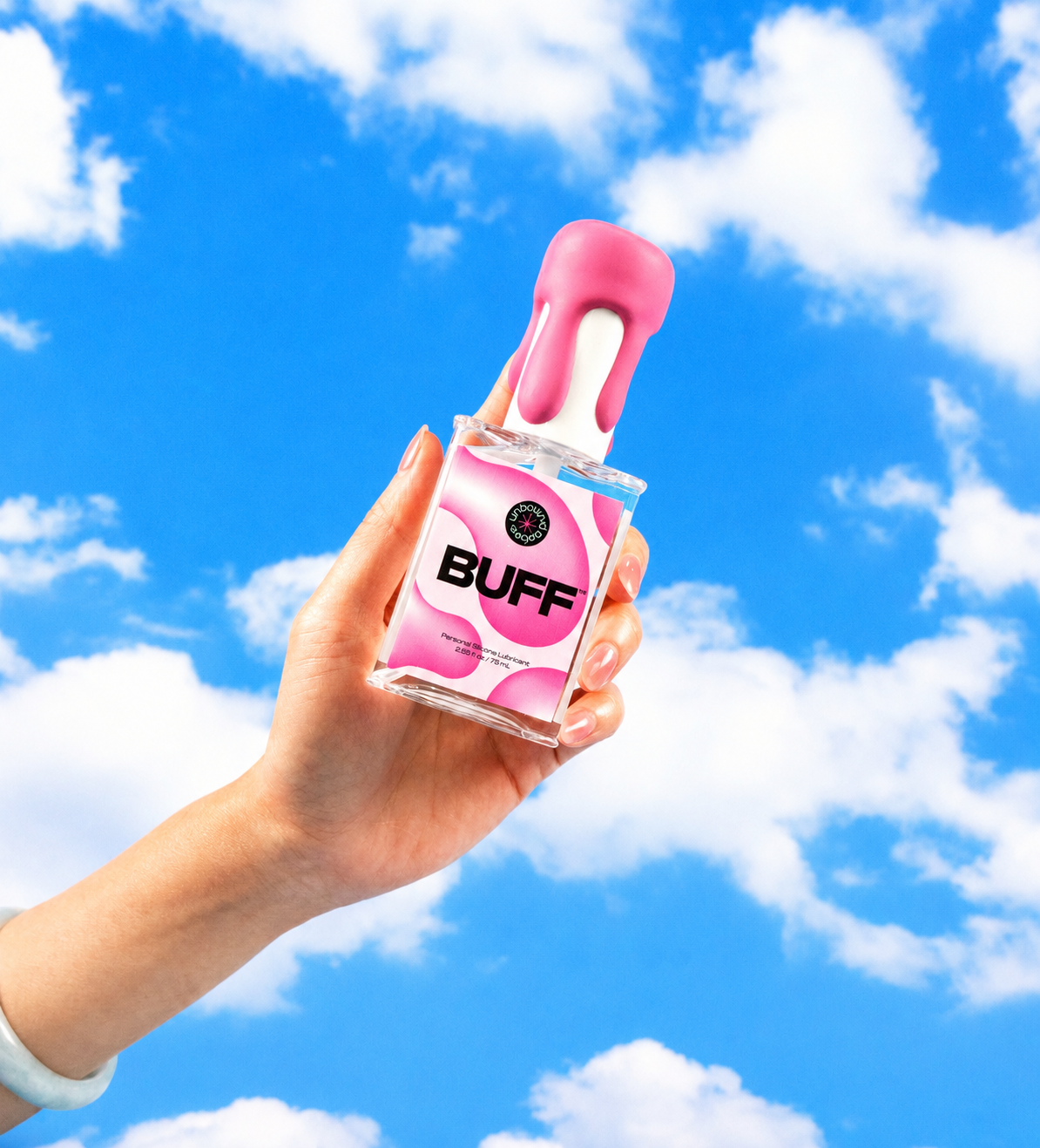 A hand holding a clear bottle of pink liquid with a pink cap against a bright blue sky with white clouds. The bottle label reads 'BUFF'.