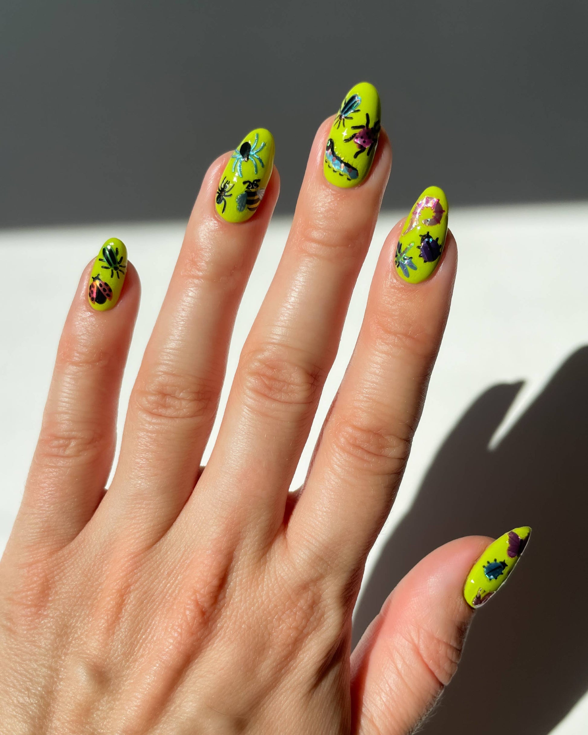Hand with neon green nails featuring black and red designs against a neutral background