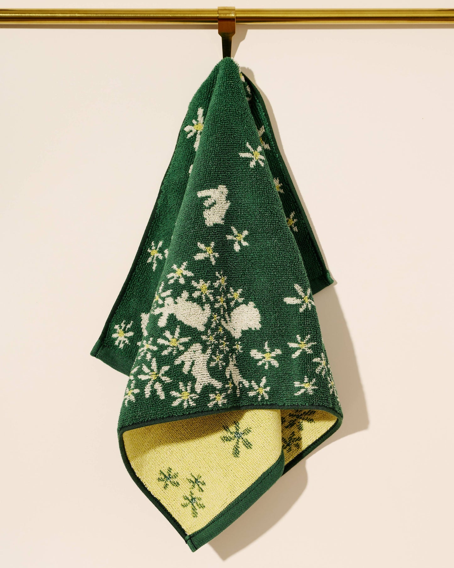 Green towel with white floral pattern hanging on a gold rod against a beige background