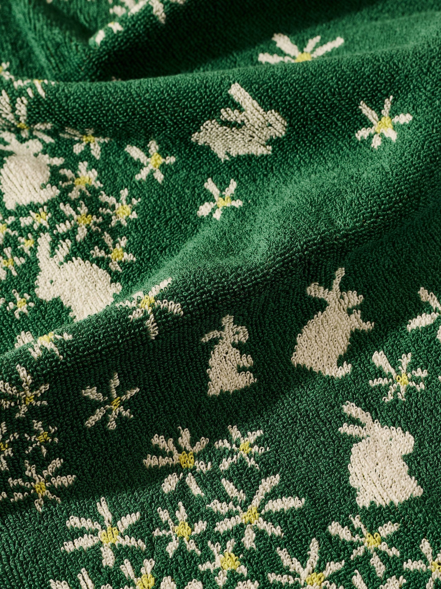 Close-up of green fabric with embroidered pattern of deer and flowers.