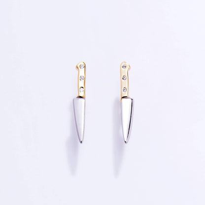 Pair of knife-shaped earrings with gold tops and silver blades on a light purple background