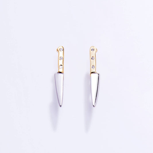 Pair of knife-shaped earrings with gold tops and silver blades on a light purple background