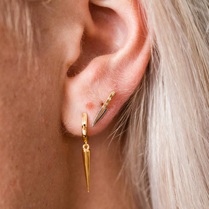 Close-up of a person wearing gold hoop earrings with dangling pendants.