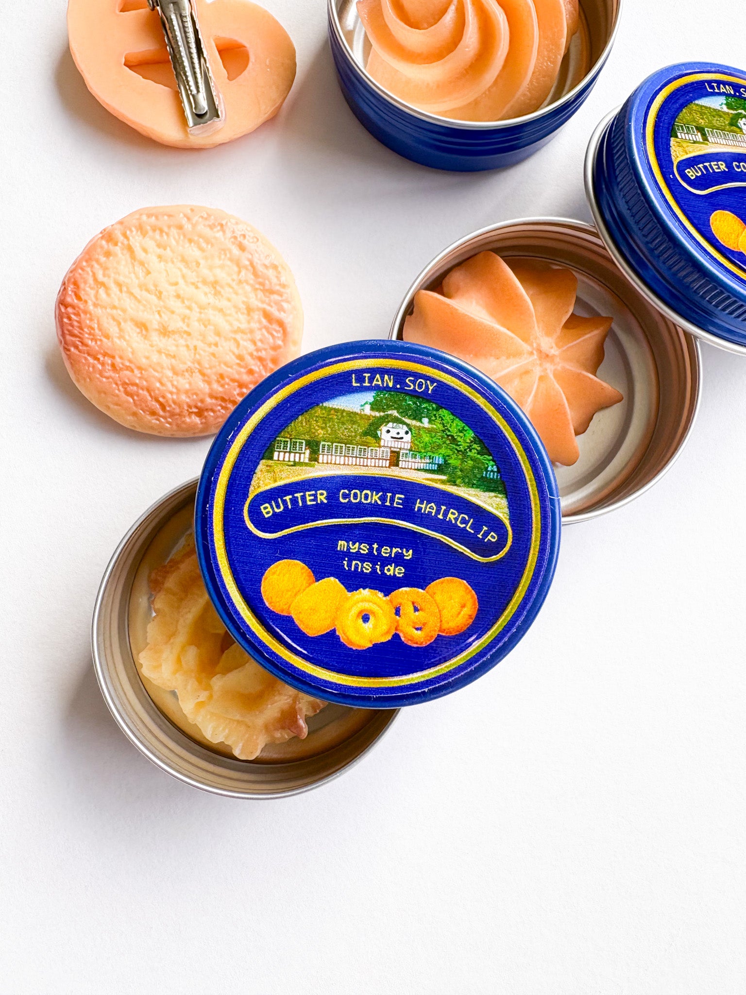 Butter cookie hairclips in open containers with blue lids on a white background