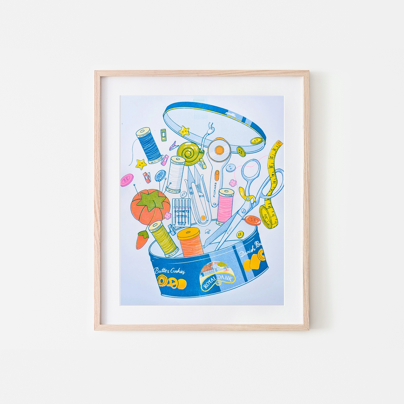 Framed illustration of a sewing kit on a white wall, Butter Cookie Sewing Supplies Risograph Art Print, Christina Hu