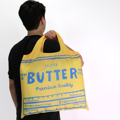 Person holding a yellow 'Butter' branded bag against a white background