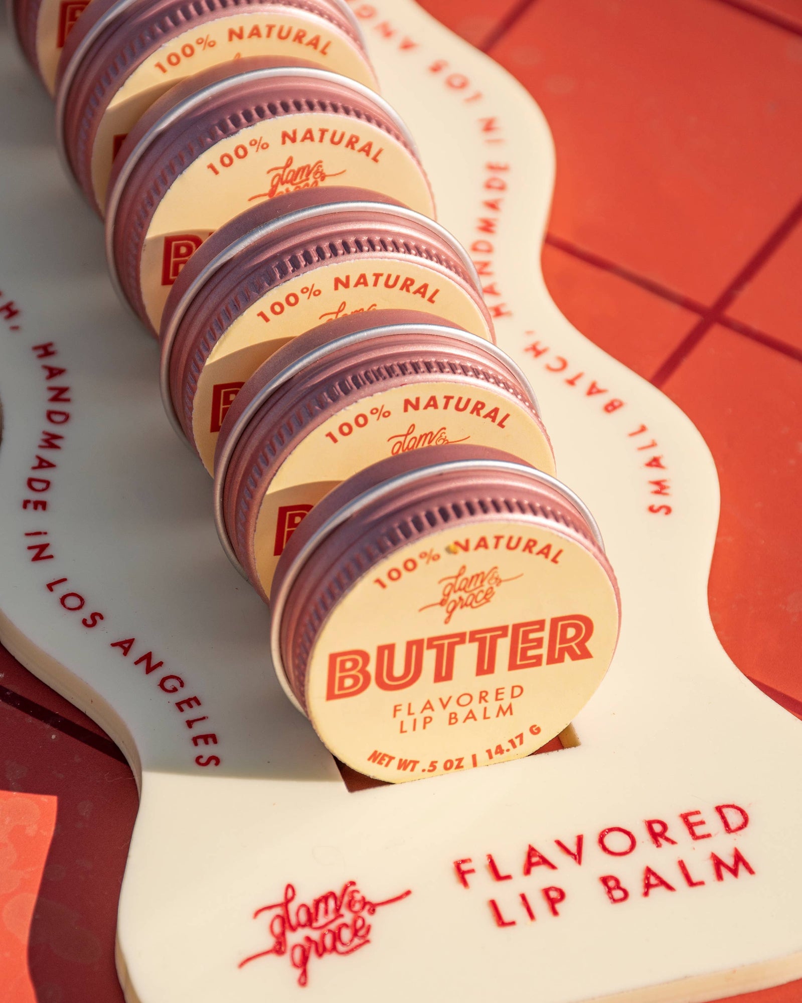 Lip balm containers on a wooden holder with 'Small Batch' branding.