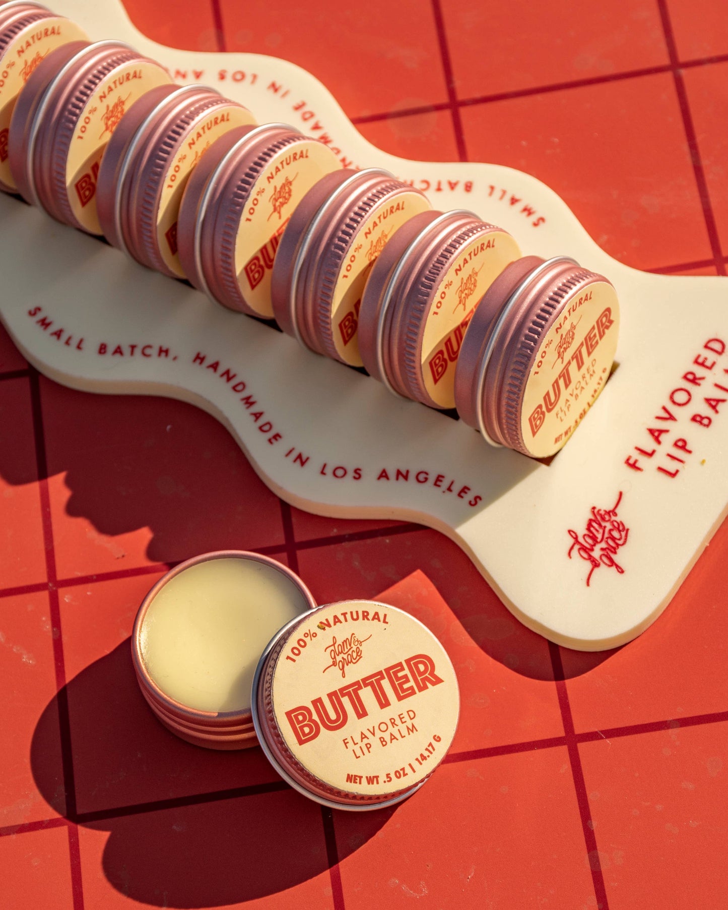 Butter lip balm containers on a red grid background