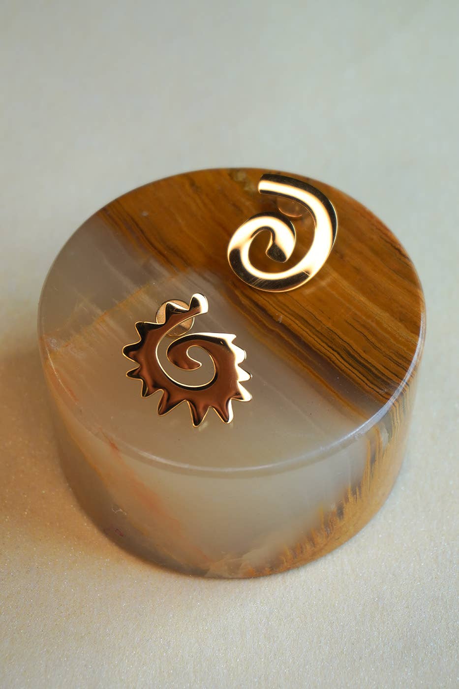 Round decorative item with a gold spiral design on a beige background