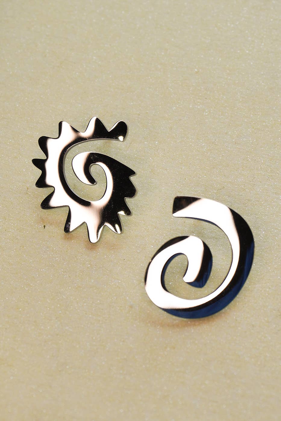Two silver spiral earrings on a beige background