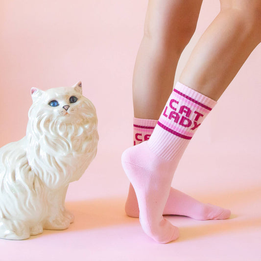 Person wearing pink socks with 'CAT LADY' text next to a white cat-shaped object on a pink background