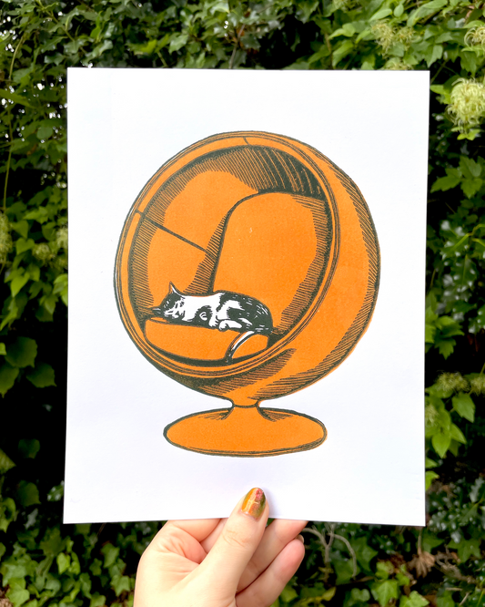 Illustration of a cat in an orange sphere held against a green leafy background