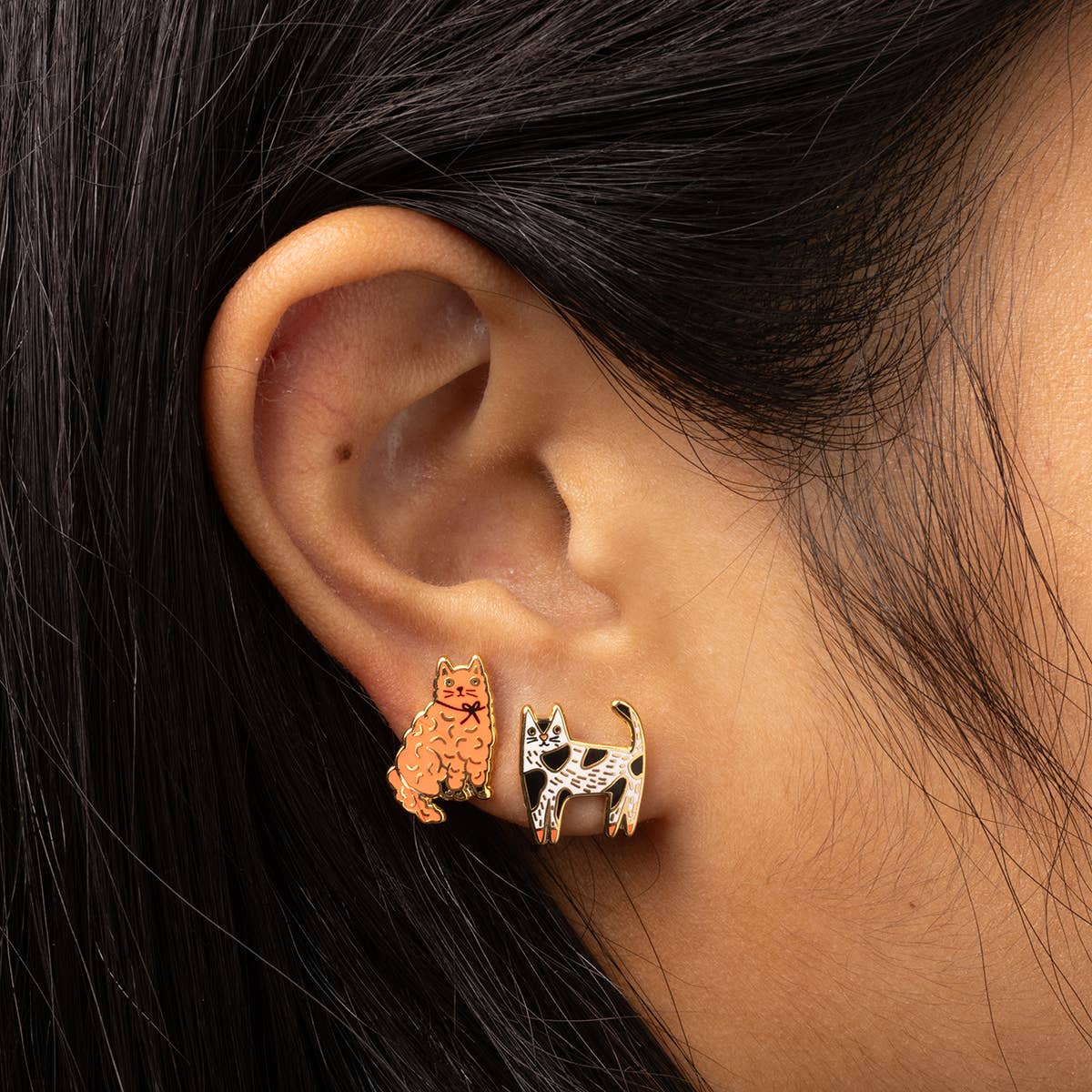 Close-up of an ear wearing gold cat-shaped earrings with a dark background