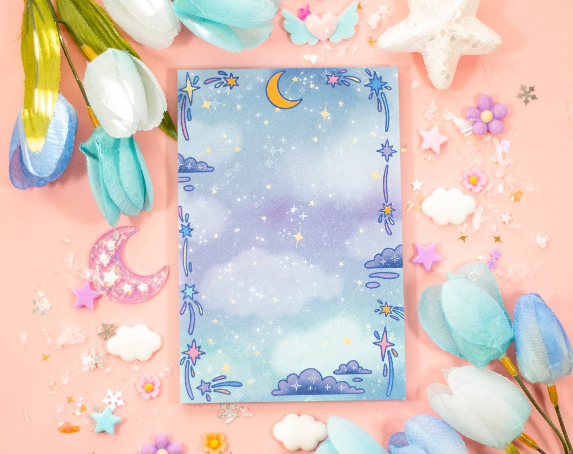 Notebook with celestial moon design surrounded by flowers on a pink background