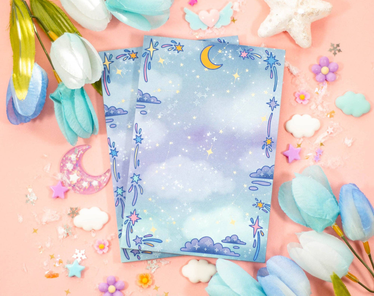 Two colorful notepadswith star and moon designs on a pink background with decorative elements.
