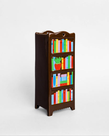 A miniature dark brown wooden bookshelf with colorful toy books and a small potted plant, shown on a plain light gray background.
