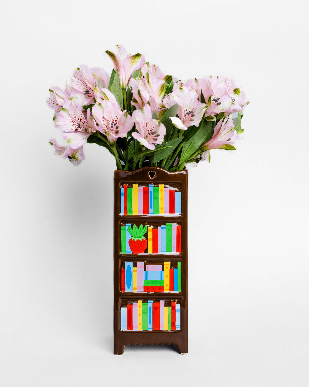 A decorative miniature bookshelf vase filled with pink alstroemeria flowers, set against a plain white background.
