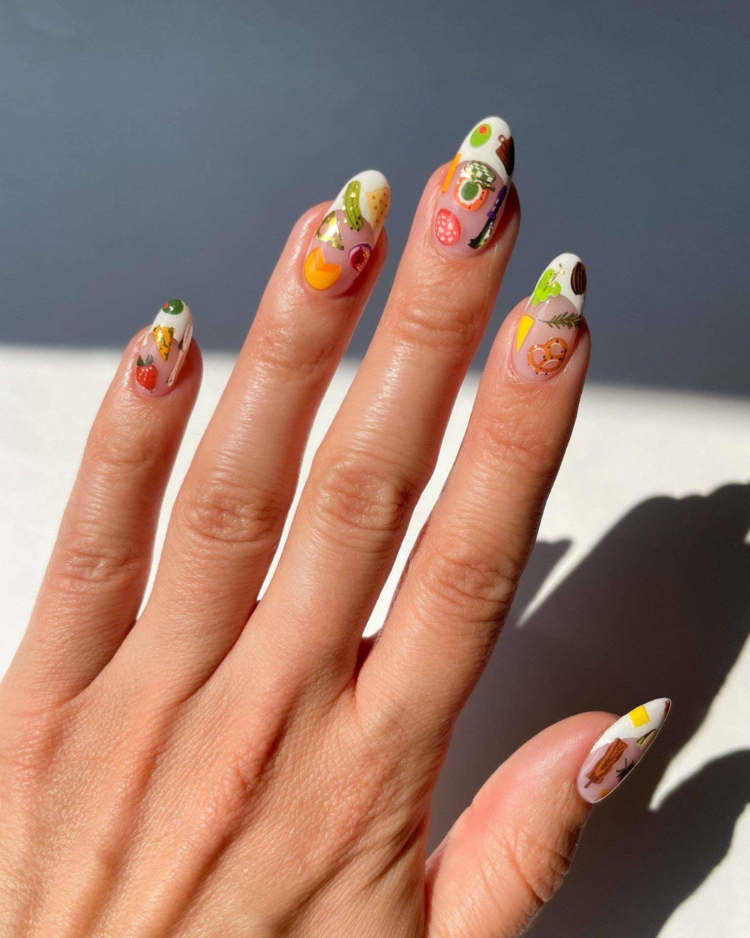Hand with intricately designed nails featuring cartoon characters against a neutral background. Charcuterie Nail Art Stickers, deco beauty