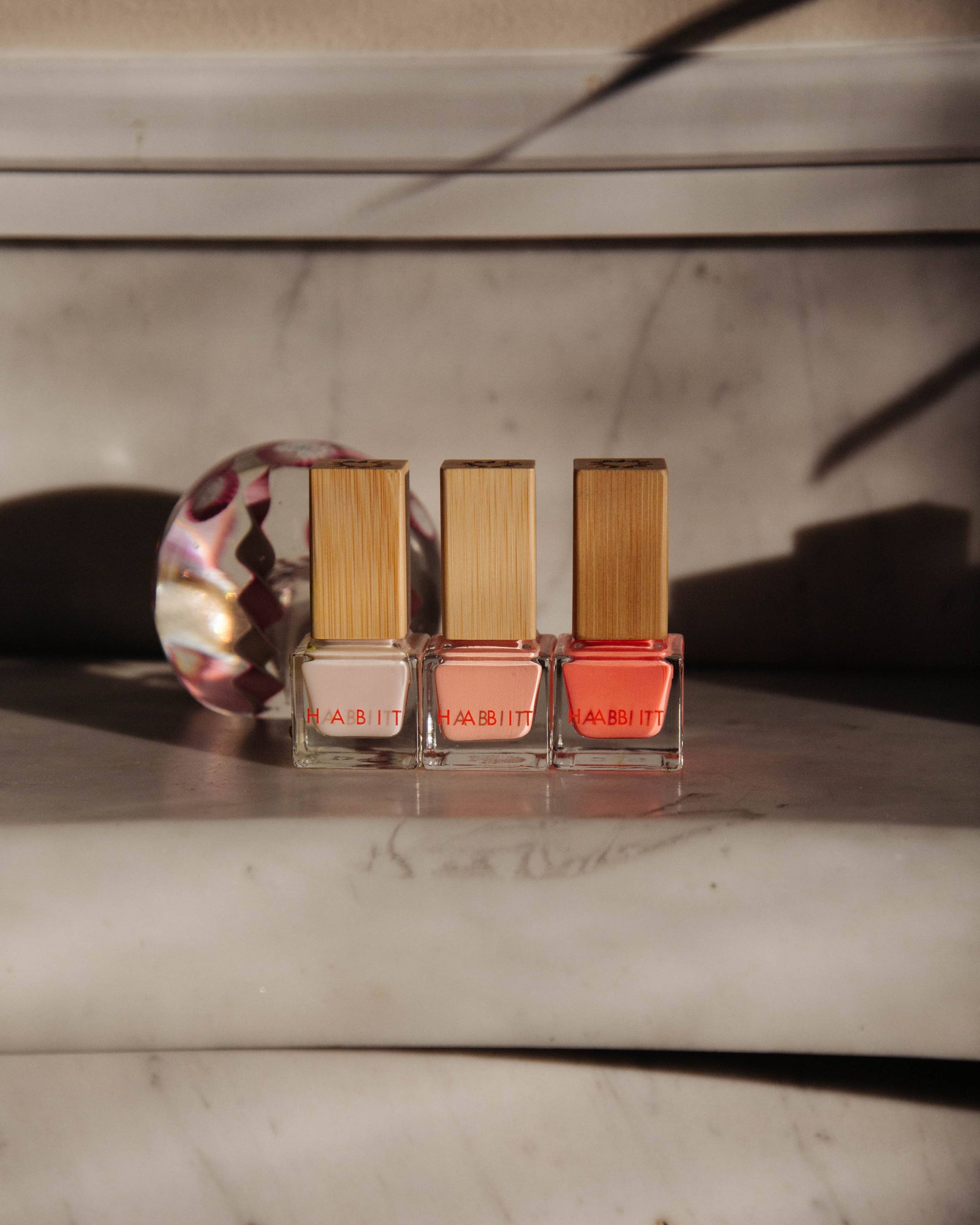 Three nail polish bottles with wooden caps on a marble surface