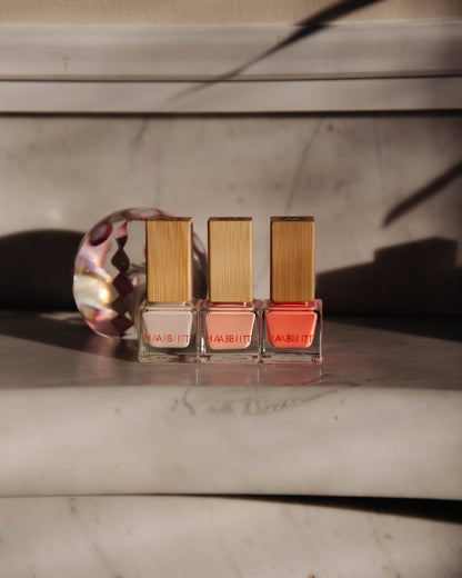 Three nail polish bottles with wooden caps on a marble surface