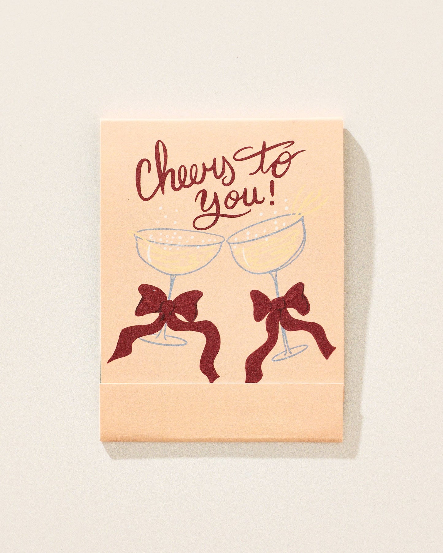 Card with 'Cheers to you!' text and two champagne glasses with bows on a beige background