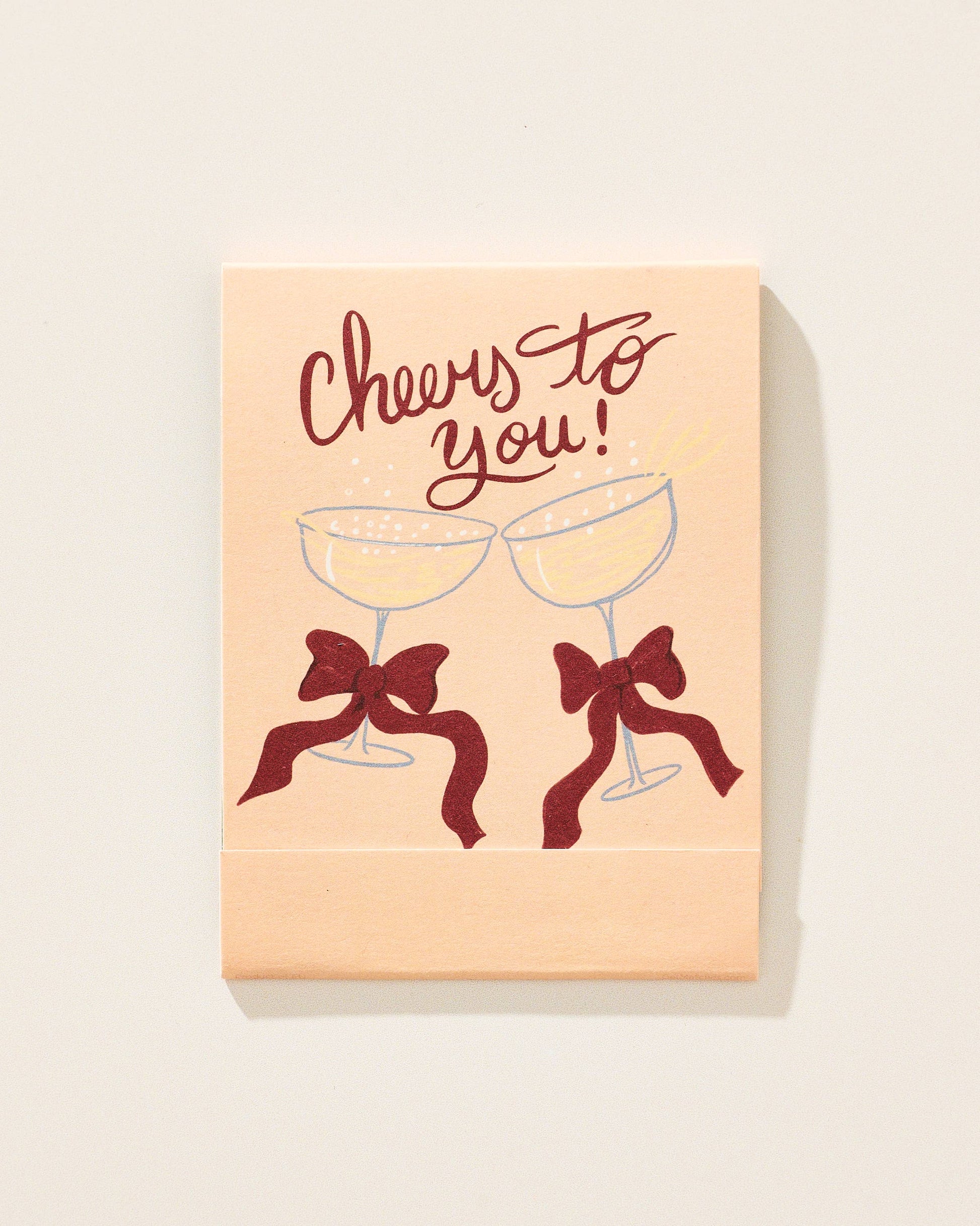 Card with 'Cheers to you!' text and two champagne glasses with bows on a beige background