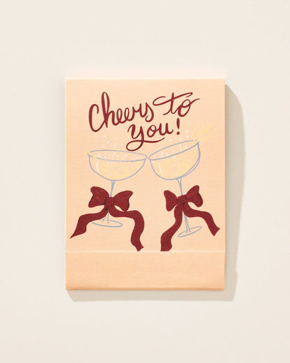 Card with 'Cheers to you!' text and two champagne glasses with bows on a beige background