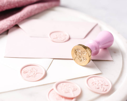 Pink wax seals on white envelopes with a gold stamp on a light pink background